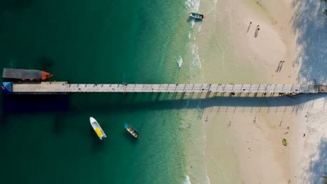 Luftbild-Von-Oben-Nach-Unten-Auf-Den-Weißen-Sandstrand-Mit-Longtail-Boot,-Das-Am-Pier-Am-4k-Strand,-Koh-Rong,-Kambodscha-Angedockt-Ist