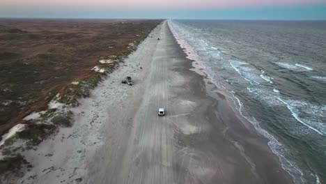 vehicles driving through the sandy shore of padre island in texas, usa - aerial drone shot