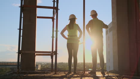 Builders-look-at-a-cityscape-on-a-sunset-background-back-view.