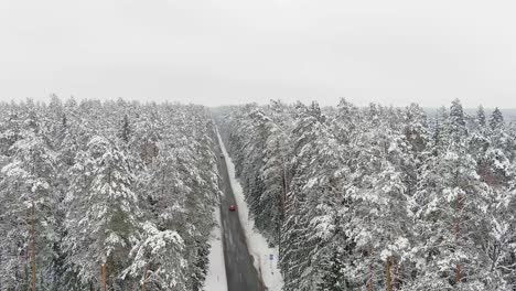 Rotes-Auto,-Das-Auf-Majestätischer-Winterstraße-Im-Litauischen-Wald-Fährt,-Luftaufstiegsansicht