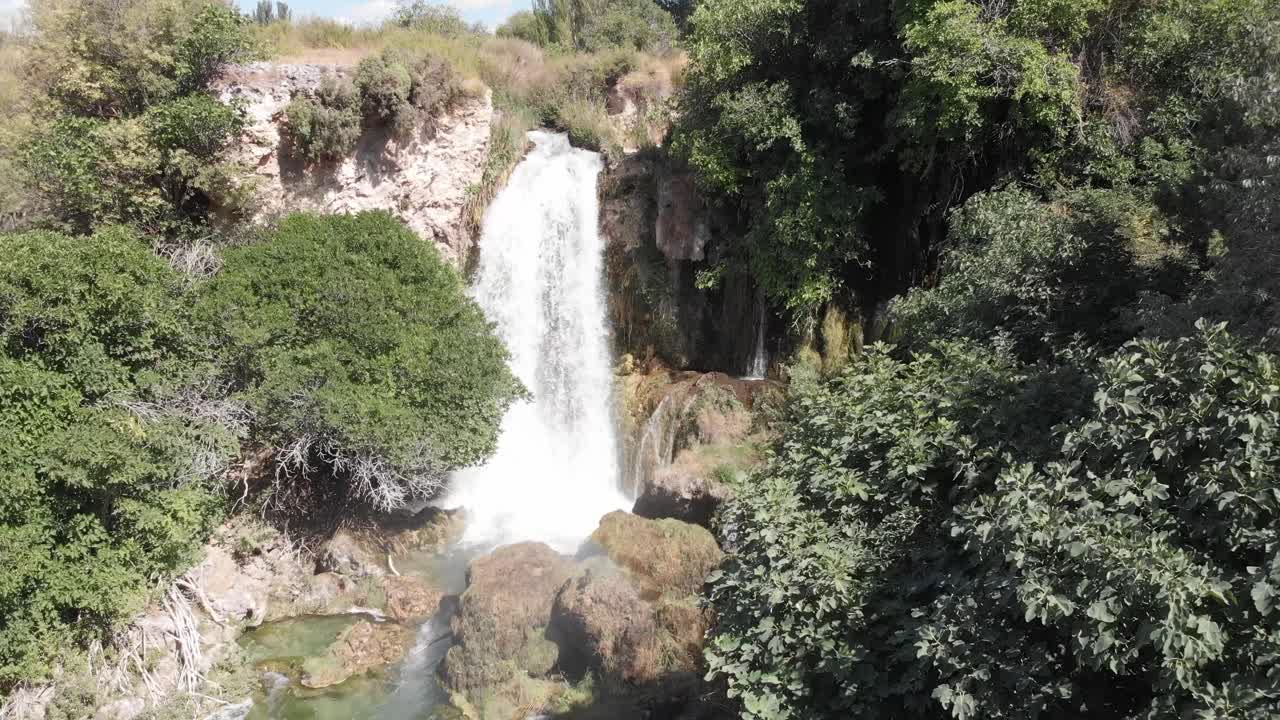 cascada salvaje que fluye desde una cornisa rocosa rodeada de árboles y crea un arco iris