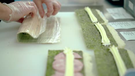 Cook-prepares-Japanese-rolls-wraps-ingredients-in-rice-and-nori-seaweed-using-a-mat