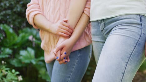 mid section of diverse female couple walking and holding hands in garden