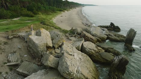 aerial establishing view of beautiful young romantic caucasian girl in a long dress on the white sand beach with old ruins, sunny summer evening, sunset, golden hour, wide drone shot moving forward