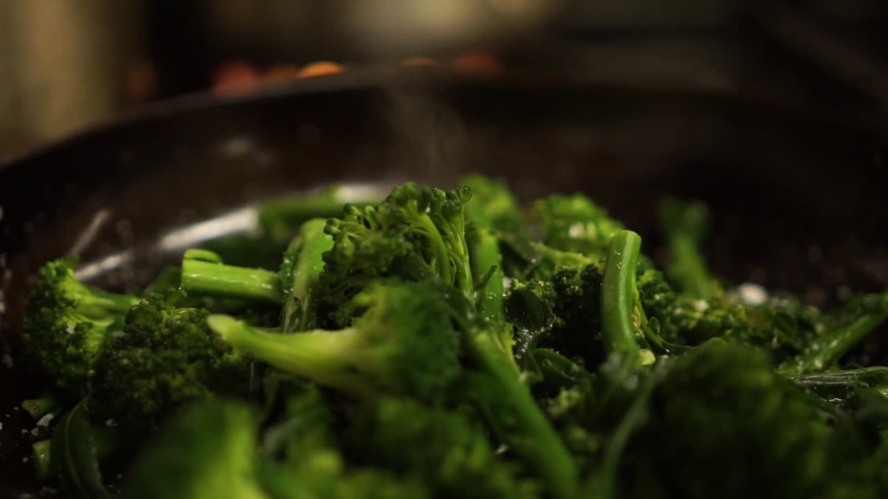 SLOWMO - Close Up - Sprinkling salt on steamed fresh green broccoli on a black frying pan