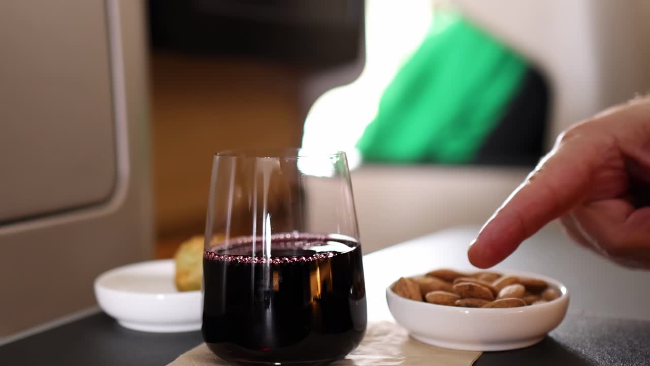 Una mano si protende verso una ciotola di mandorle accanto a un bicchiere di vino rosso su un tavolo