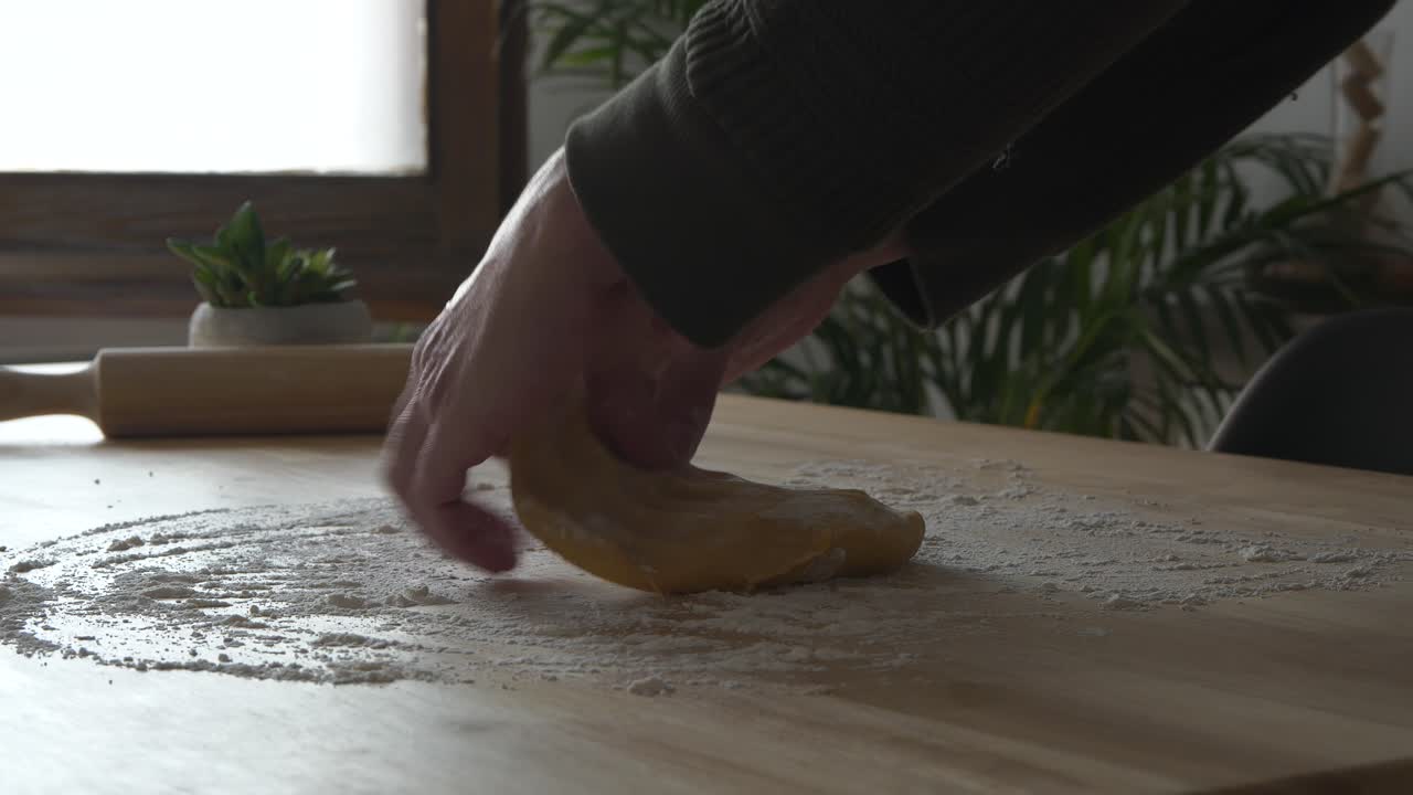 Le mani di un giovane uomo che modellano l'impasto fresco della pasta su un tavolo di legno a casa, inquadratura fissa
