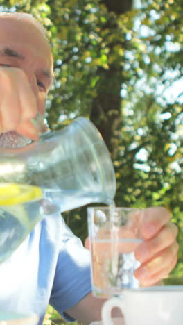 senior man pouring water in glass at garden