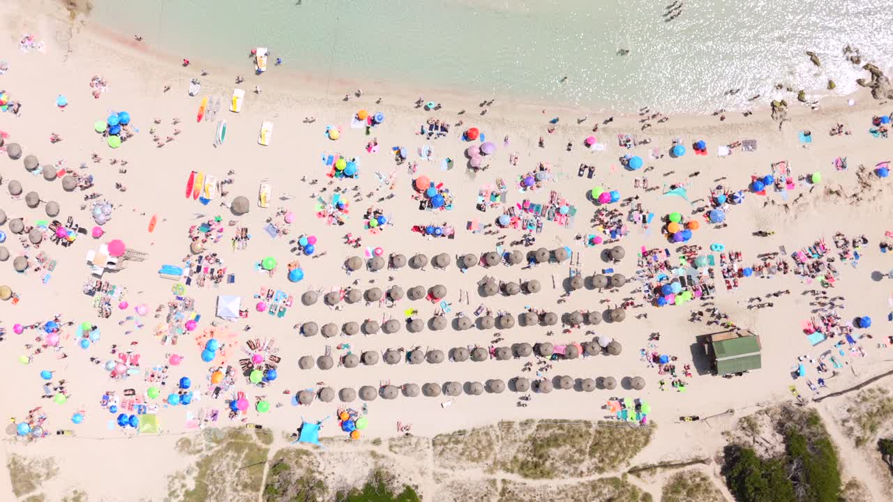 Tourists sunbathe on crowded beach with colorful umbrellas in Mallorca, aerial birds eye