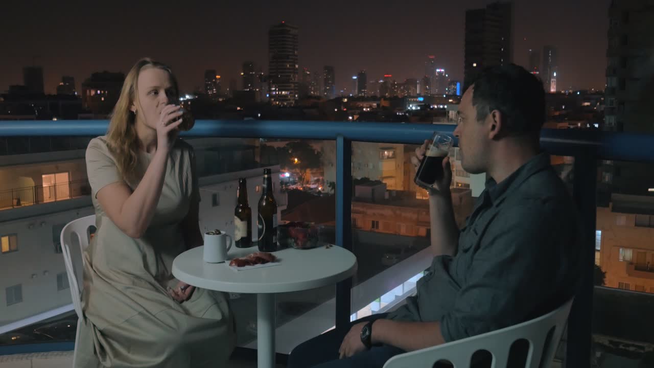 젊은 커플이 텔아비브의 야간 옥상 카페에서 휴식을 취하고 술을 마시고 있습니다.