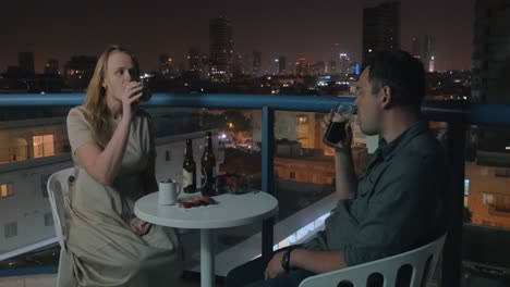 una pareja joven relajándose y tomando bebidas en la azotea del café de la noche de tel aviv.