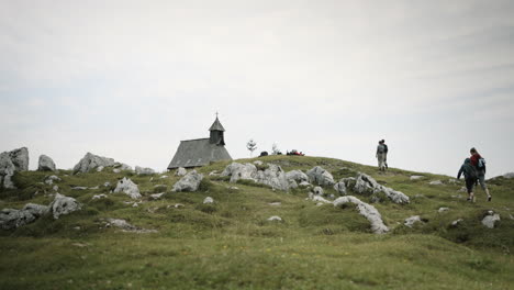 people walking towards the church on the top of mountain velika planina, rocks sticking out of the earth