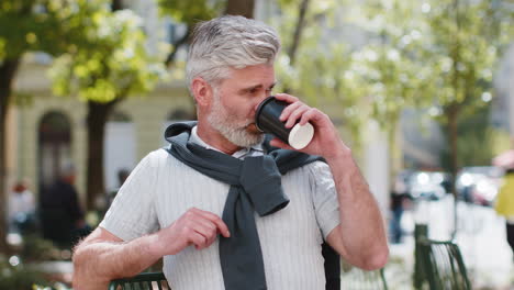 mature man enjoying morning coffee hot drink relaxing taking a break sitting on cafe chair on street