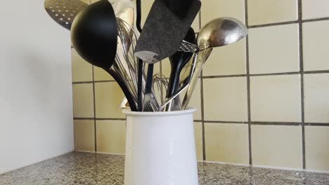 varios utensilios de cocina, como un batidor de cucharón o una espátula, se colocan en una cacerola blanca en una cocina con su flujo en el fondo