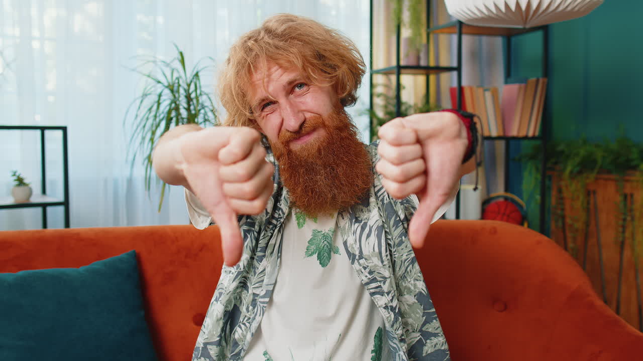 Upset caucasian man showing thumbs down dislike bad work disapproval dissatisfied feedback at home