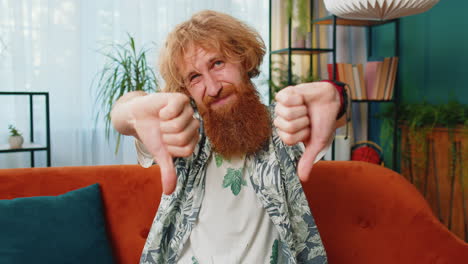 Upset caucasian man showing thumbs down dislike bad work disapproval dissatisfied feedback at home