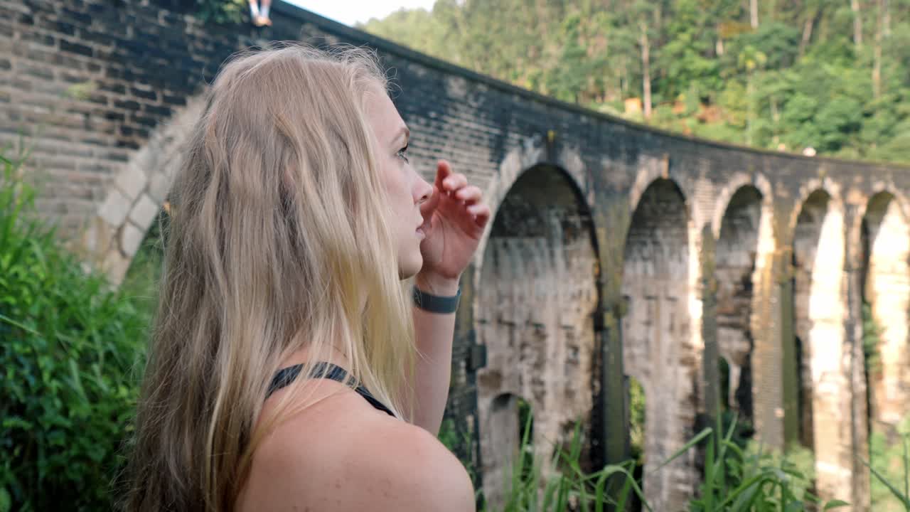 A young woman observes the historic Nine Arch Bridge from a nearby hillside in Ella, Sri Lanka.