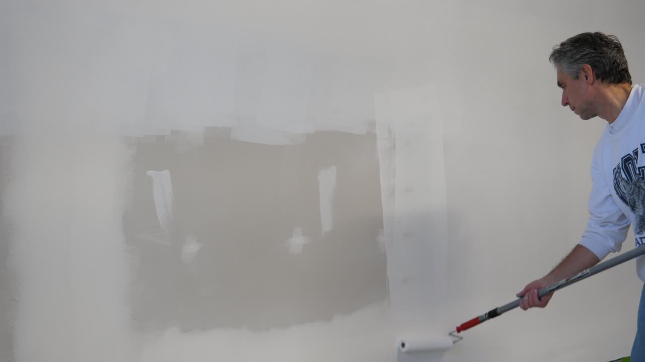macho adulto aplicando imprimación a paneles de yeso - rodillo de pintura pintura blanca - construcción