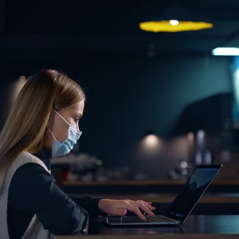 working woman prints something on her laptop. female employee sitting at the desk in dark room. blurred backdrop