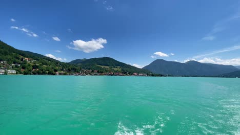 the popular bavarian tegernsee, having a trip over the turqouise water at summertime, filmed from a ship looking backward to the impressive water color with the alps in the background