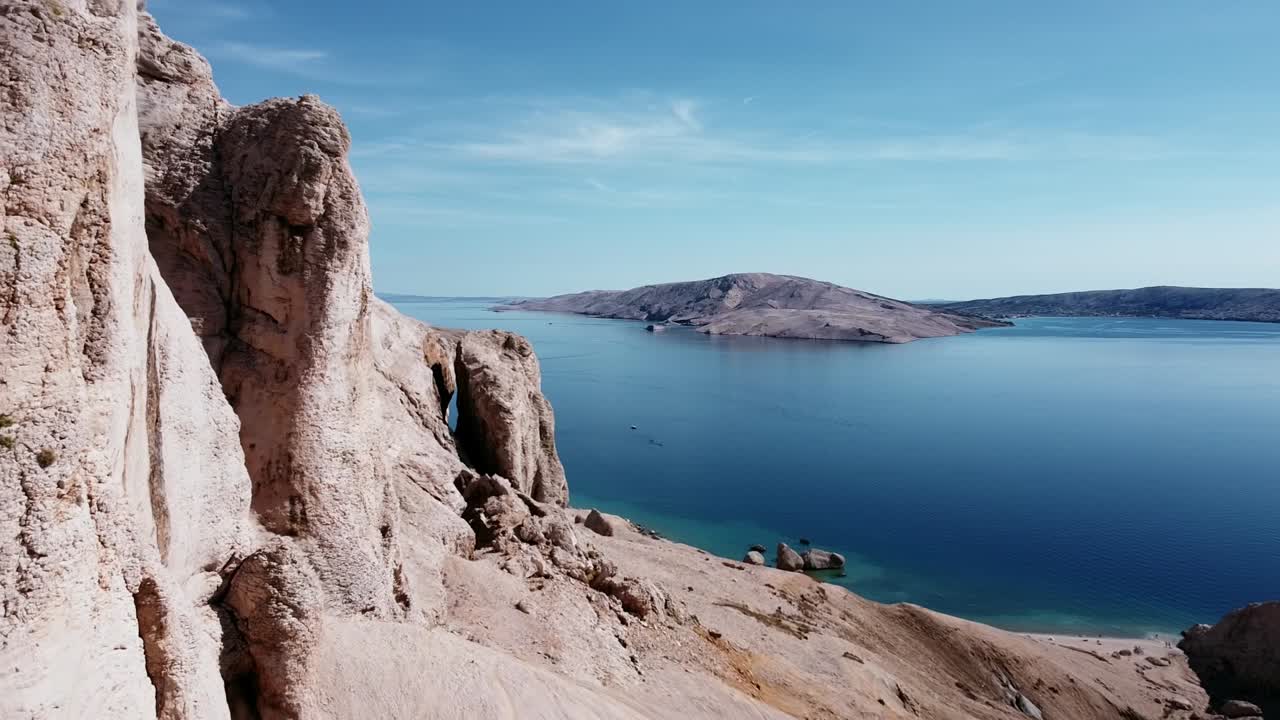 vuelo de drones cerca de montañas rocosas a la izquierda y mar azul al fondo