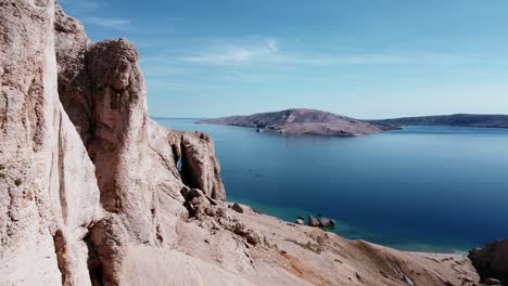 vuelo de drones cerca de montañas rocosas a la izquierda y mar azul al fondo