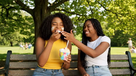 two young women enjoying ice cream together on a park bench