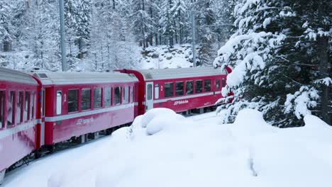 view of a red train passing through a forest and a winter snow covered landscape