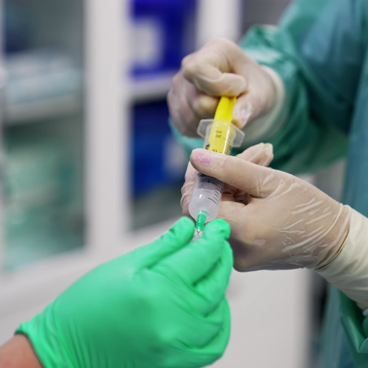 Medics in latex gloves taking medicines into syringe from a little bottle. Doctors at operation in modern surgery room. Blurred backdrop