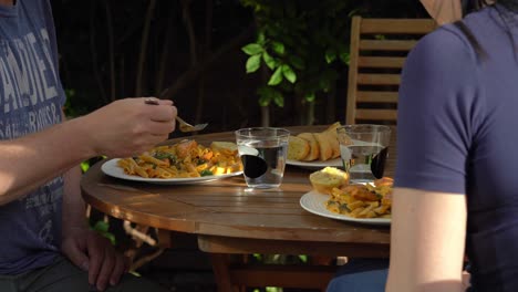 couple enjoying a delicious pasta chicken meal with bread and water outdoors in garden