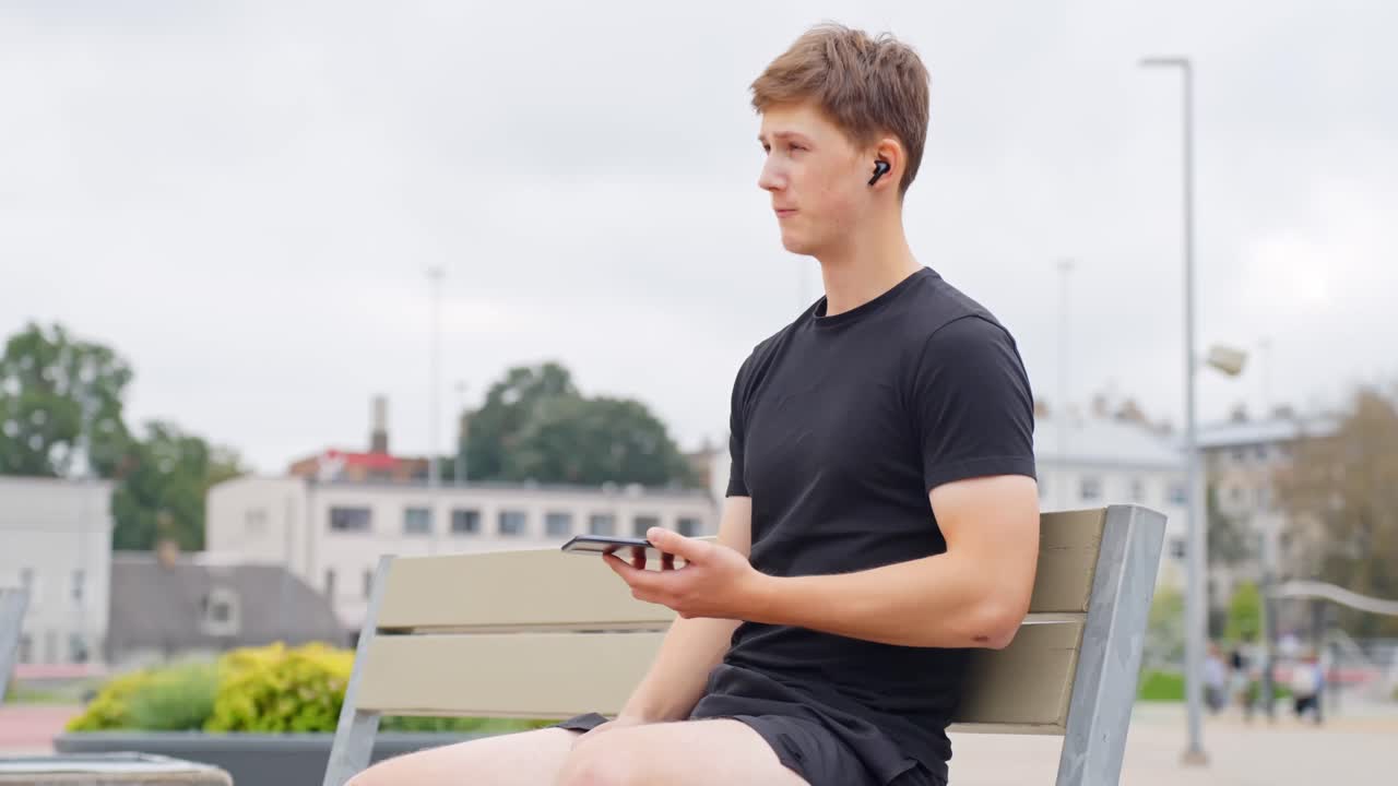 Smiling guy sitting on a park bench making a call with his smartphone