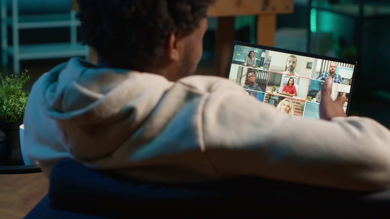 Focused young man smiling and waving during a web conference at his home, showcasing online communication in a digital and wireless lifestyle. Conference speaker with attendees. Camera A.