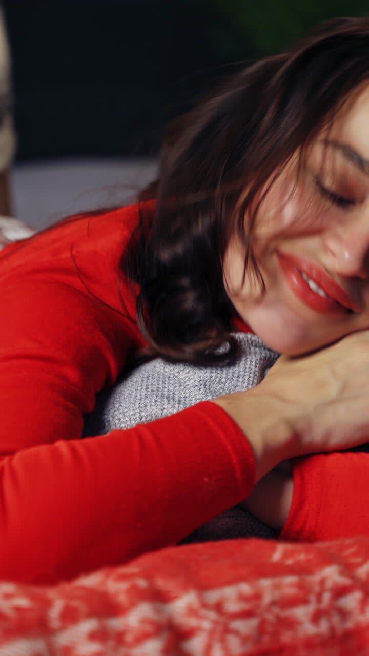 Happy girl on bed at Christmas. Young woman on bed resting at home with pillow at New Year time. Joyful mood of a pretty female at Christmas. Vertical video