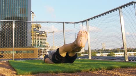 Tattoed-Guy-is-doing-Exercises-on-a-terrace-in-front-of-a-big-Tower-in-Vienna-during-sunset,-4K