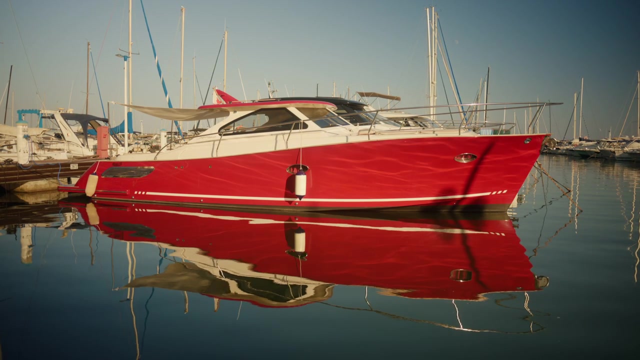 Motoscafo di lusso rosso ormeggiato in un porto turistico, che si riflette sull'acqua calma, circondato da altre imbarcazioni e cielo sereno