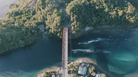 Vista-Aérea-Del-Puente-De-Acero-Sobre-El-Agua-Azul-Turquesa-Con-Barcos-De-Pesca-Locales-Navegando-En-Un-Pequeño-Pueblo-De-Pescadores-En-El-Sur-De-Leyte,-Filipinas---Tiro-Aéreo-Ascendente-De-Drones,-Tiro-De-Retroceso