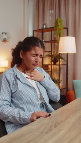 indian woman freelancer feeling unwell sick suffering from sore throat touches neck coughing at home