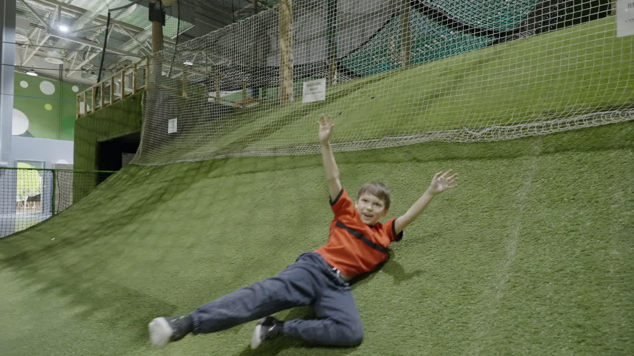 Boy climbs and slides on a green wall in an indoor playground