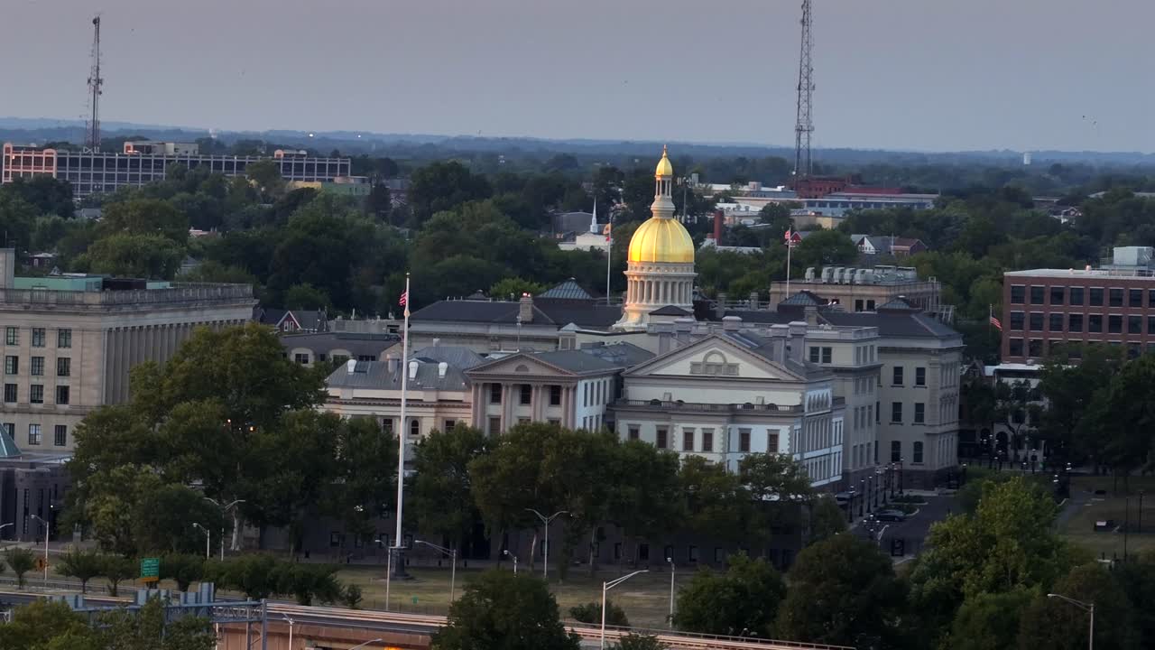 New Jersey State Capitol with golden cupola, with american flag ion flagpole in front yard. Dusk scene in Trenton, New Jersey. Aerial wide shot