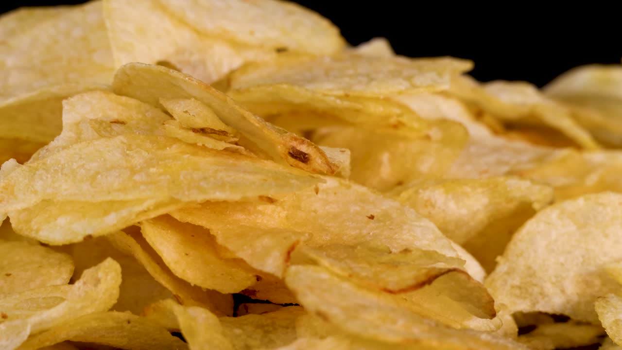 Camera slowly zooms in on golden potato chips against black background, crisp texture highlighted