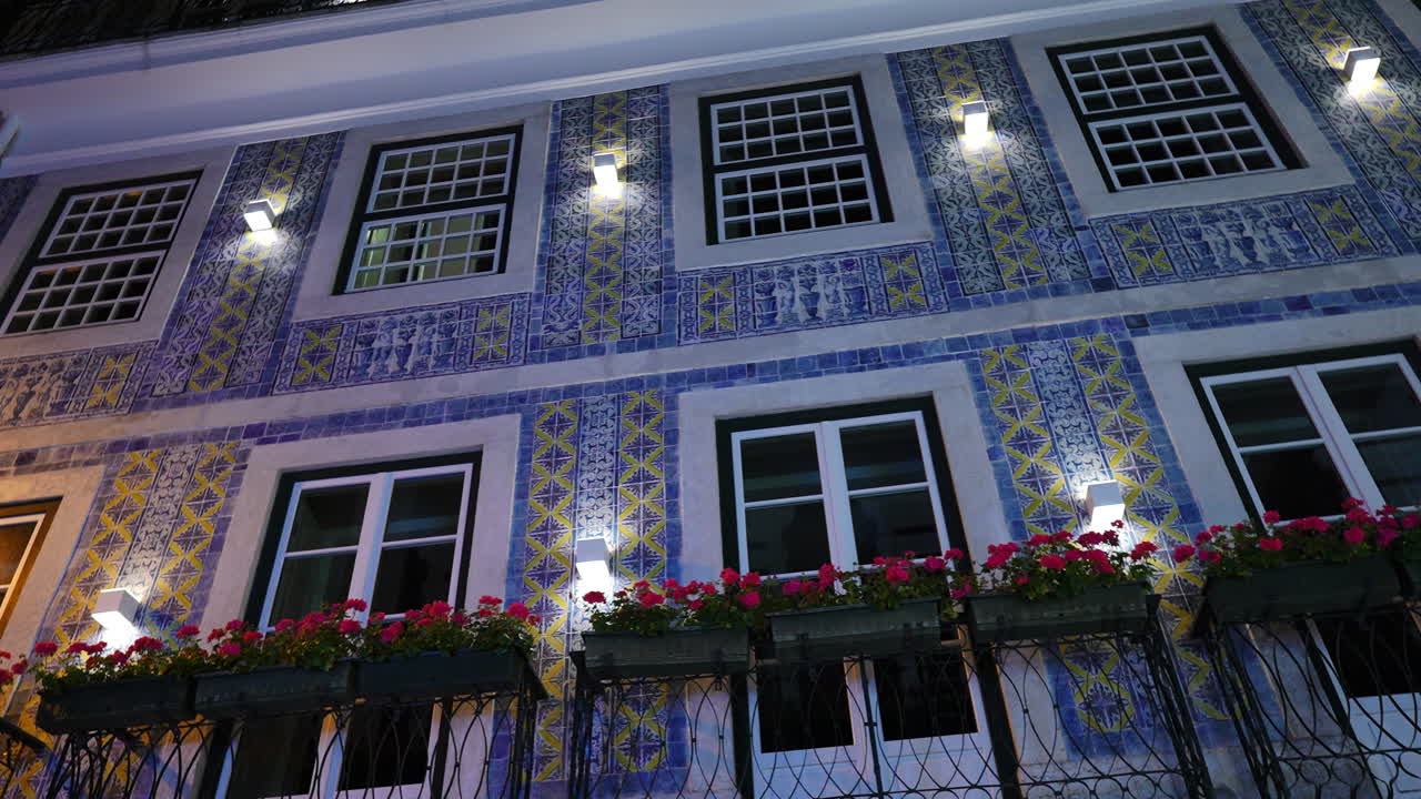 Vibrant blue and yellow ceramic azulejos adorning Portuguese building facade, glowing under nighttime illumination in historic Lisbon streetscape