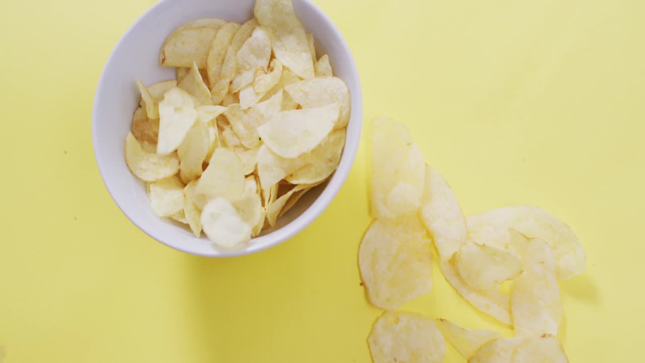 Close up of potato chips falling in a bowl on yellow surface