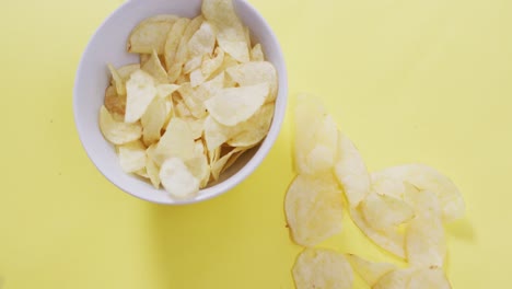 Nahaufnahme-Von-Kartoffelchips,-Die-In-Eine-Schüssel-Auf-Einer-Gelben-Oberfläche-Fallen