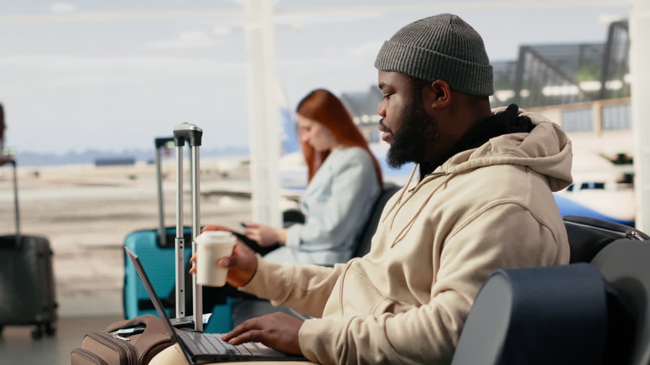 African American Man Working on Laptop and Drinking Coffee in Airport Lounge