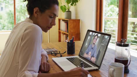 Afroamerikanische-Frau-Macht-Sich-Notizen,-Während-Sie-Zu-Hause-Einen-Videoanruf-Auf-Dem-Laptop-Führt