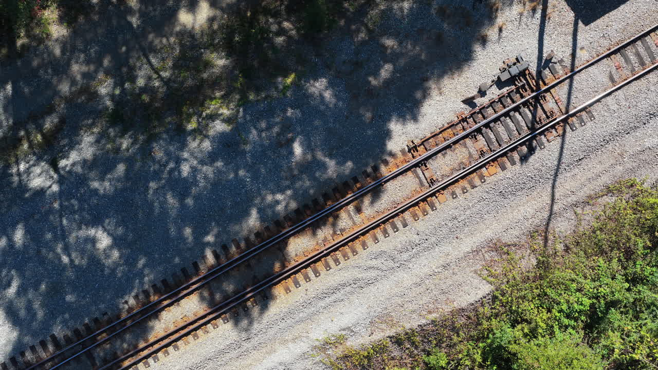 Ascesa aerea di binari ferroviari coperti di ghiaia con le ombre degli alberi della foresta, Benton, Arkansas.
