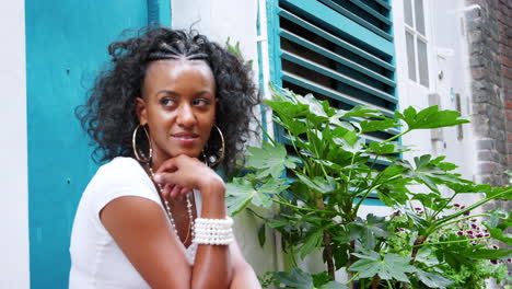 fashionable young black woman sitting in a doorway looks to camera and laughs, close up