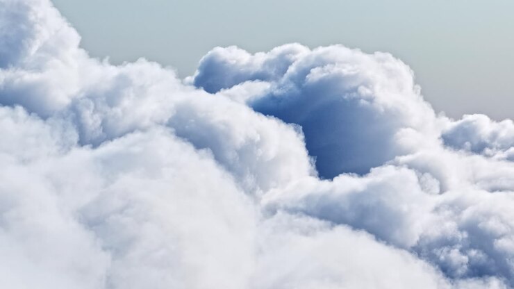 A smooth timelapse above the cloud layer, showing soft, rolling, bright-white formations shifting and swelling in the sunlight, creating a dreamy and airy atmosphere