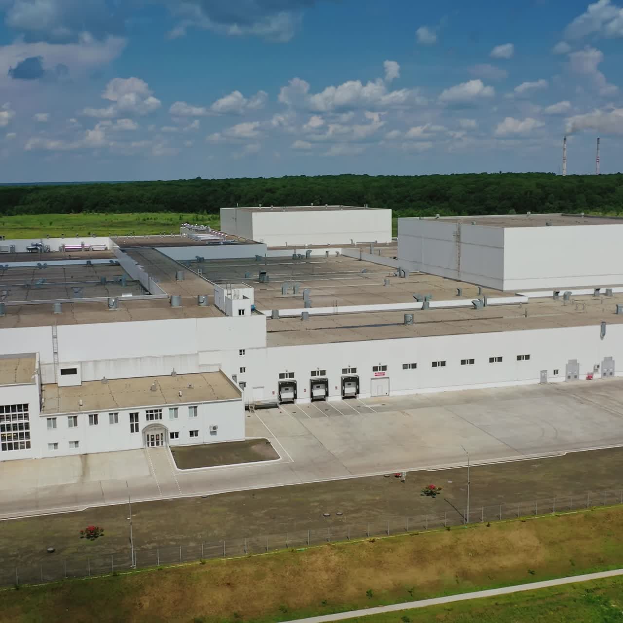 Modern manufacture under blue sky. Industrial plant among field. New large agriculture buildings. Drone side view.