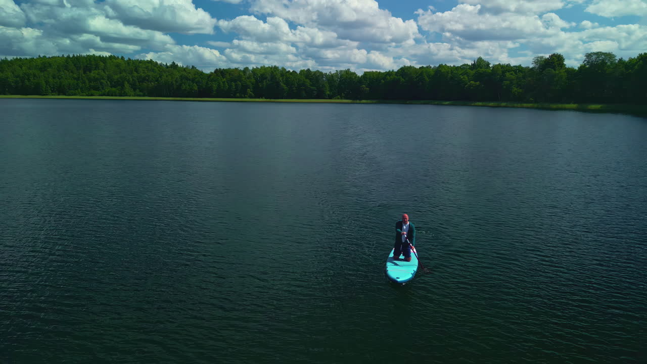 hombre arrodillado en stand-up paddleboard, remando en un lago tranquilo